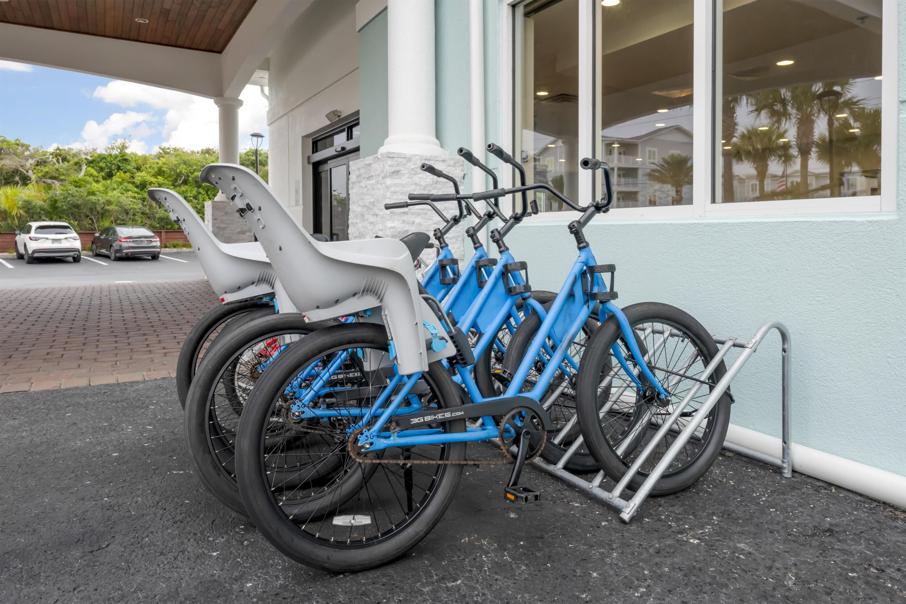 A row of blue bicycles parked outside a building with a white exterior and large windows.
