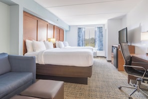 A hotel room with two beds, a sofa, a desk with a chair, a television, and a window with curtains.