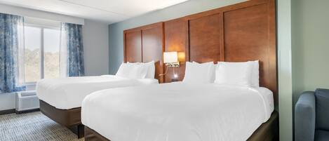 A hotel room with two beds, a nightstand with a lamp, a window with curtains, and a view of the outdoors.