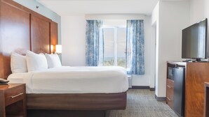 A hotel room with a bed, a television, a desk, and a window with curtains. - Surf and Sand, BW Signature Collection (Fernandina Beach)
