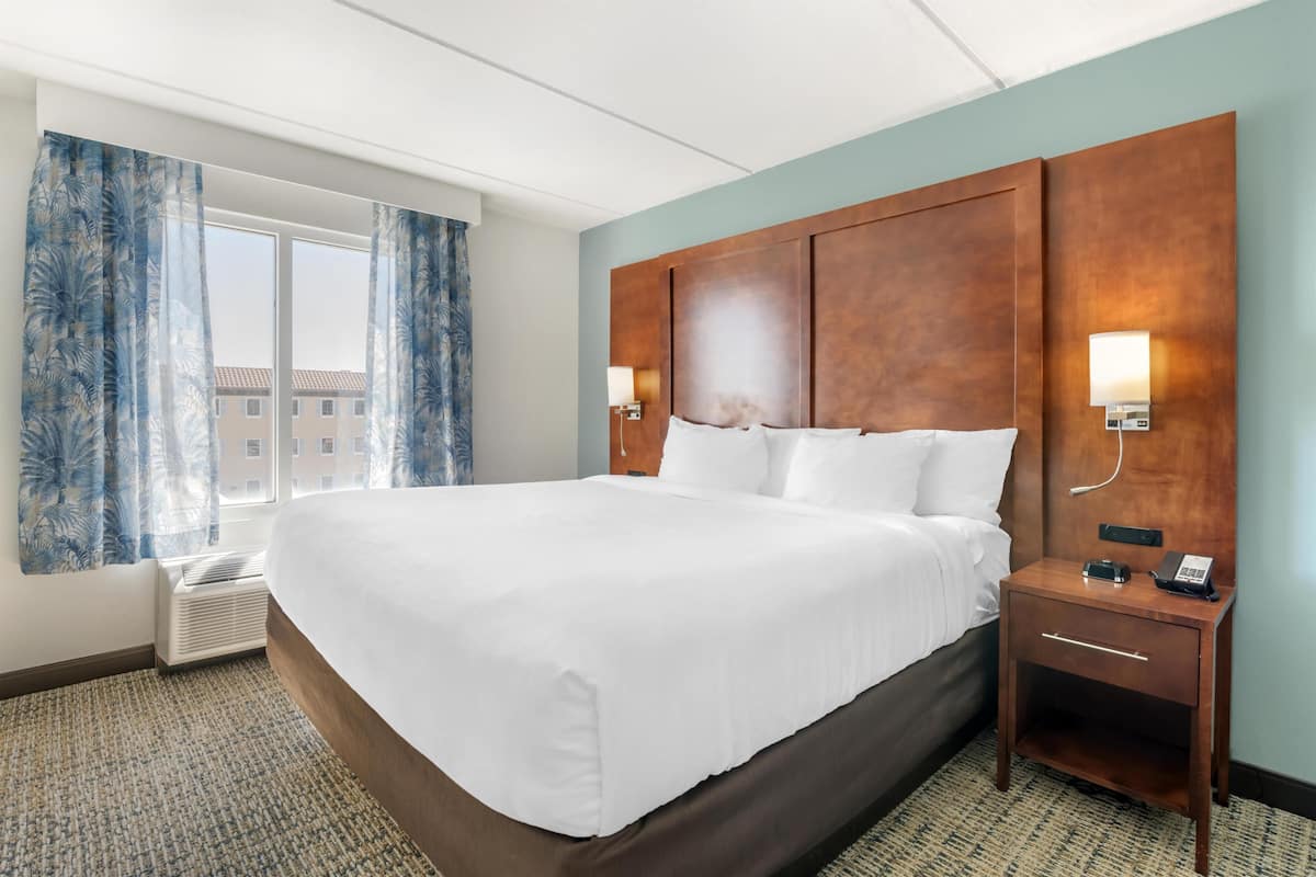 A hotel room with a large bed, a nightstand with a phone, and a window with curtains.