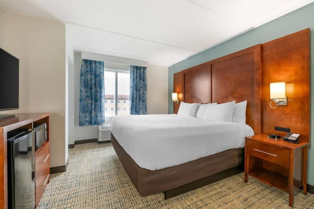 A hotel room with a large bed, a TV, a desk with a lamp, and a window with curtains.