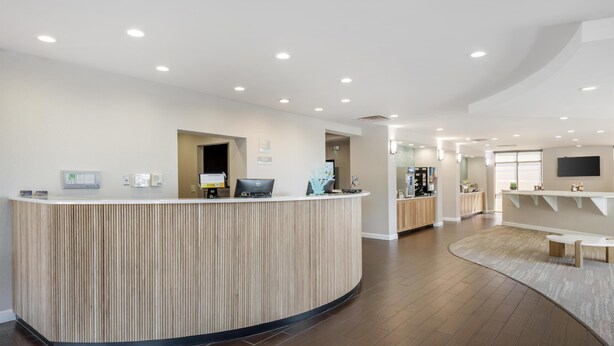 A reception desk with a laptop, a small plant, and a wall-mounted clock. - Surf and Sand, BW Signature Collection (Fernandina Beach)