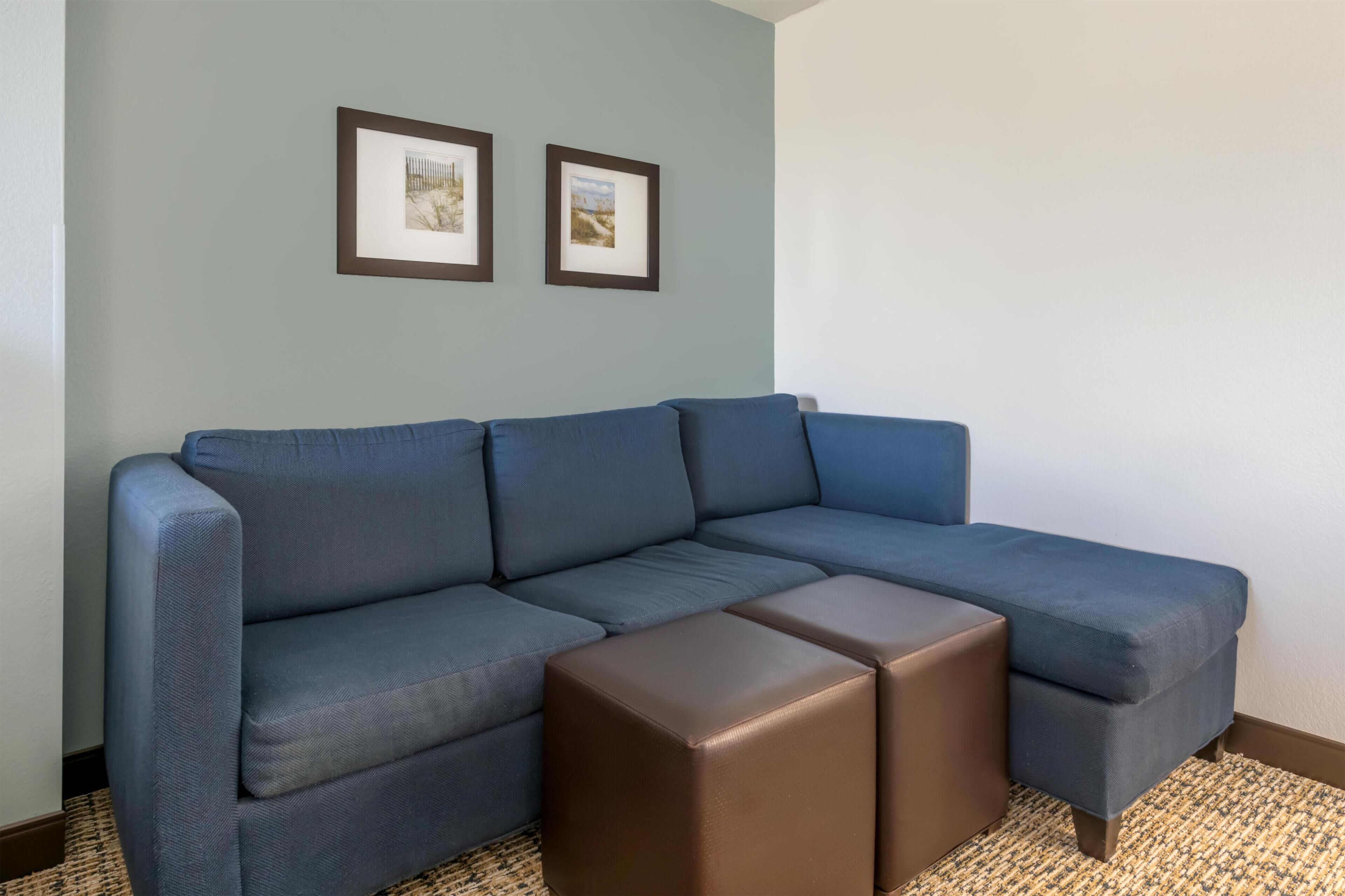 A sectional sofa with a brown ottoman, a framed picture on the wall, and a patterned rug.
