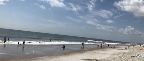 A beach with people walking and playing in the water.