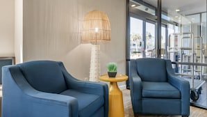 Two blue armchairs, a small round table with a plant, and a tall lamp in a modern room with large windows. - Surf and Sand, BW Signature Collection (Fernandina Beach)