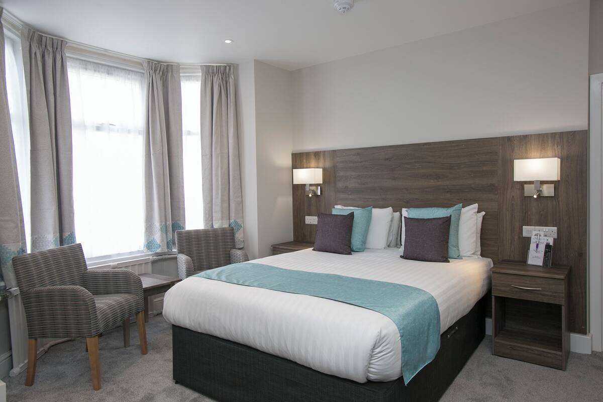 A hotel room with a large bed, two bedside tables with lamps, a chair, and a window with curtains.