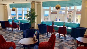 A hotel lobby with seating areas, a large window with a view, and a plant in the center. - Marsham Court Hotel (Bournemouth)