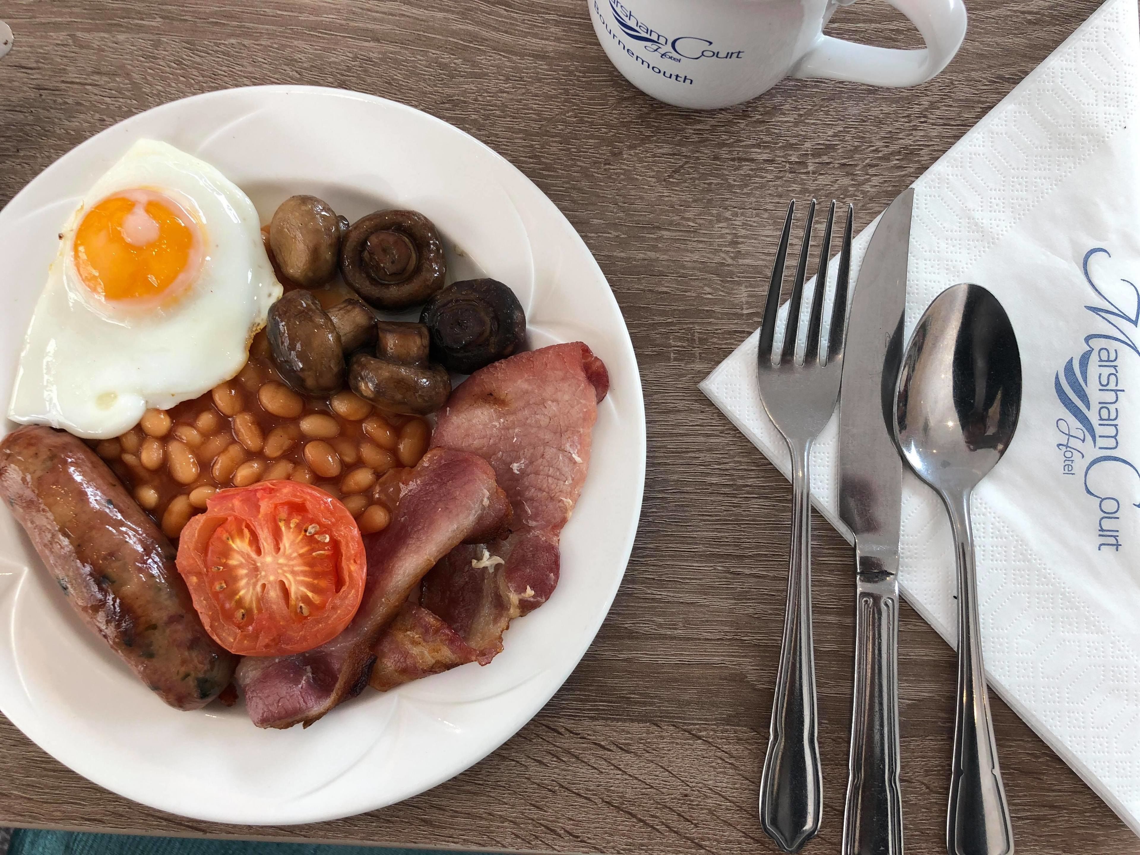 En tallerken med morgenmad, herunder æg, svampe, bønner, bacon, pølser og en tomat.