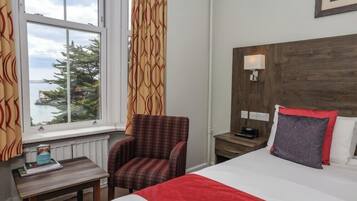 A hotel room with a bed, a chair, a nightstand, a lamp, and a window with curtains.