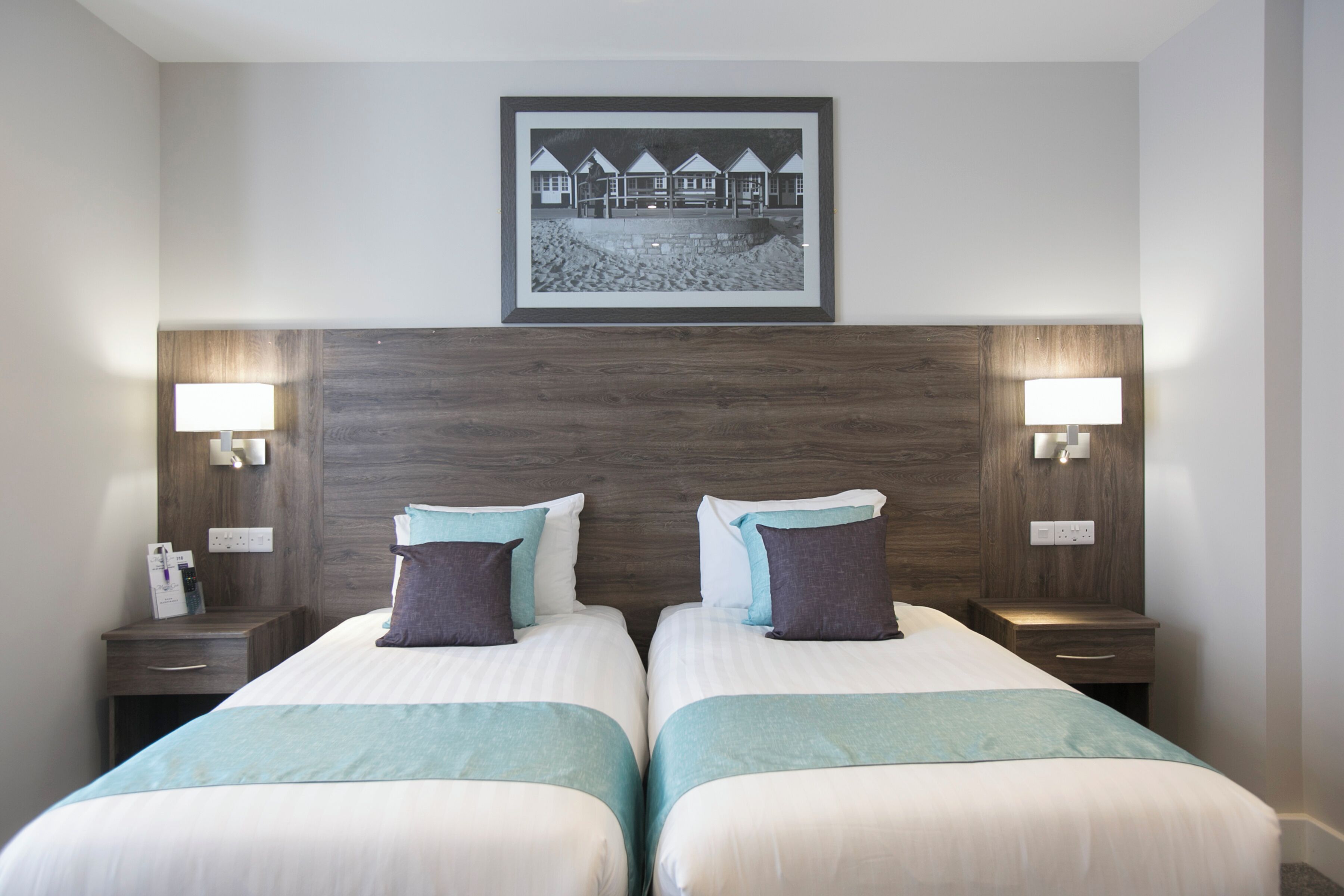 A hotel room with two beds, a framed picture on the wall, and bedside lamps.