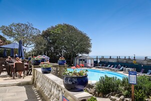 Zona junto a la piscina con sillones de descanso, plantas en macetas y vista al océano.