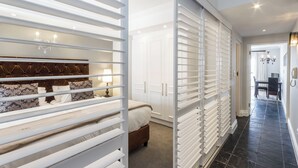 A bedroom with a bed, a nightstand, a dresser, and a sliding door closet. - Romney Park Luxury Apartments (Cape Town)