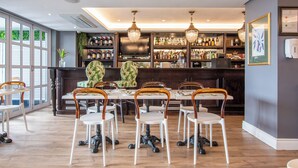 A restaurant with a bar area, wooden chairs, a large table, and a wall-mounted TV. - Romney Park Luxury Apartments (Cape Town)