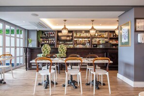 A restaurant with a bar area, wooden chairs, a large table, and a wall-mounted TV. - Romney Park Luxury Apartments (Cape Town)