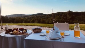 Une table de jardin, dressée pour un repas en plein air, avec de la nourriture et des boissons, et offrant une vue sur un paysage magnifique.