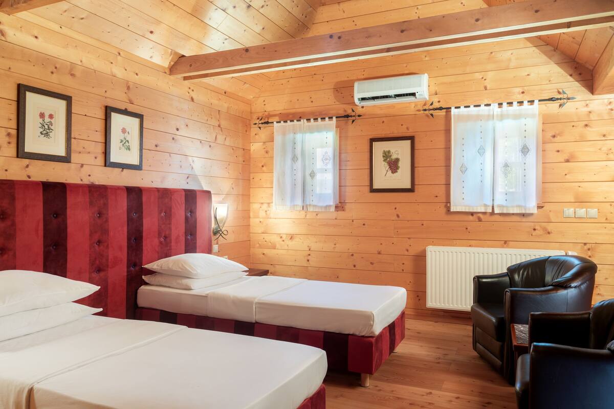 A wooden cabin with two single beds, a red upholstered headboard, a black leather chair, and framed floral artwork on the walls.