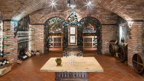 Une cave à vin aux murs de briques, aux tonneaux en bois et à la table centrale où sont disposés des verres à vin.