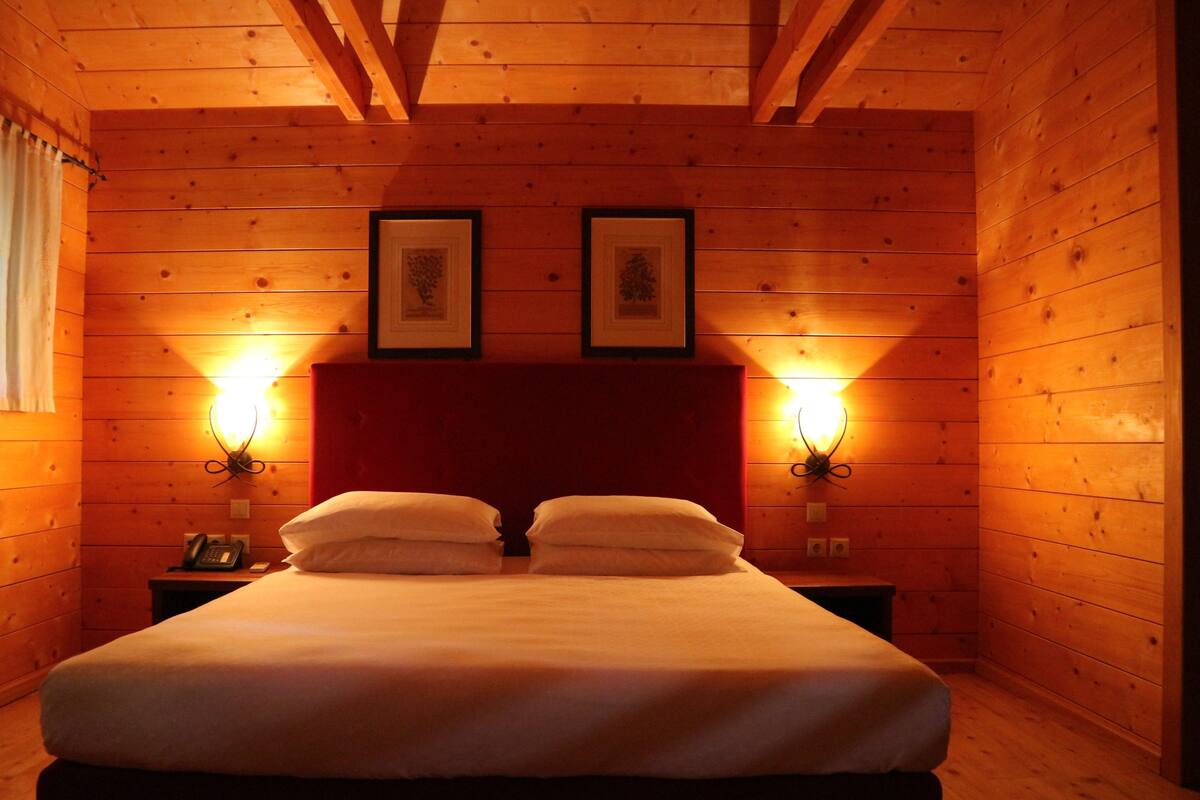 A wooden cabin-style bedroom with a bed, two wall-mounted lamps, and framed pictures on the wall.