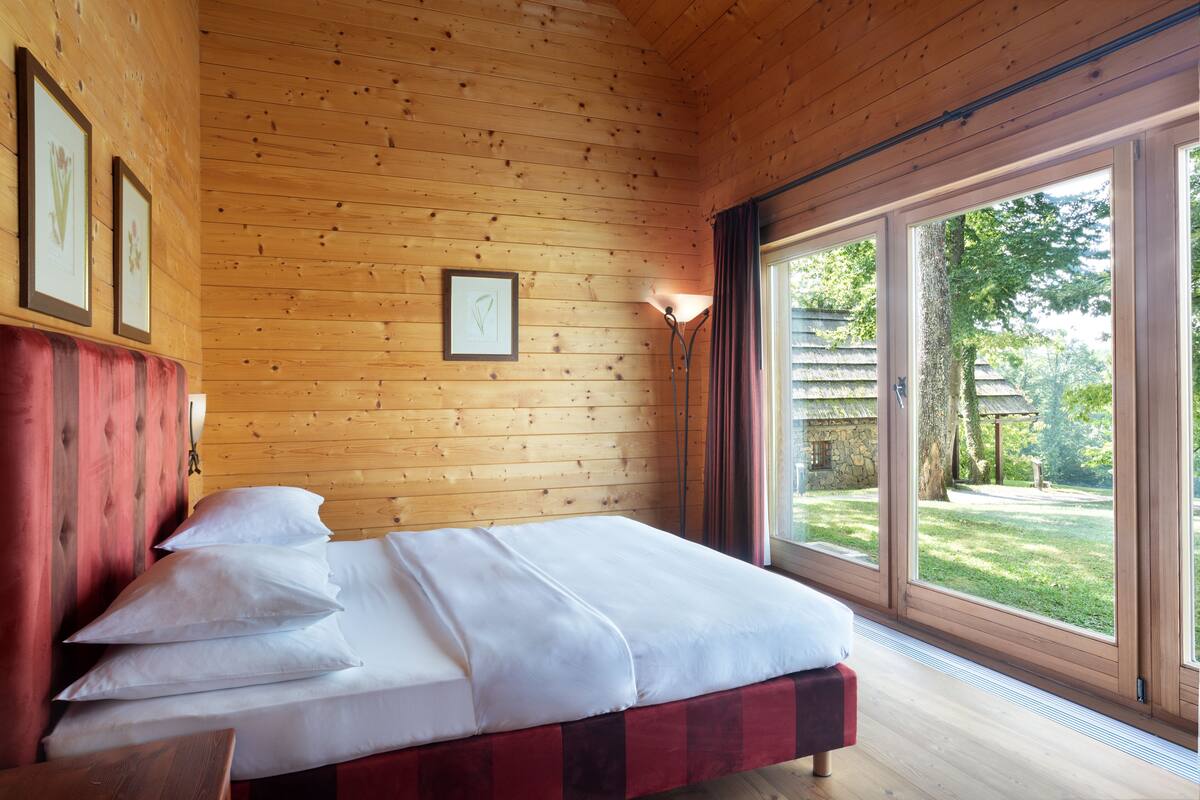 A wooden-paneled bedroom with a bed, large windows, and framed artwork on the wall.