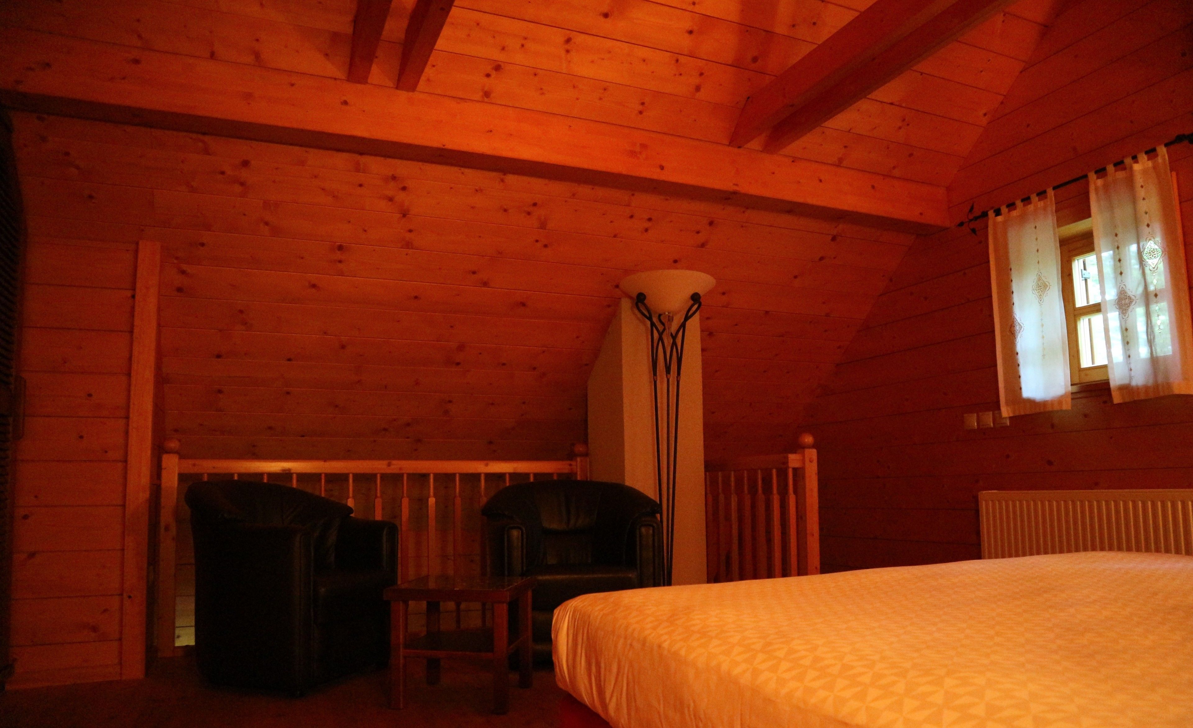 A wooden cabin room with a bed, a chair, a table, and a window with curtains.