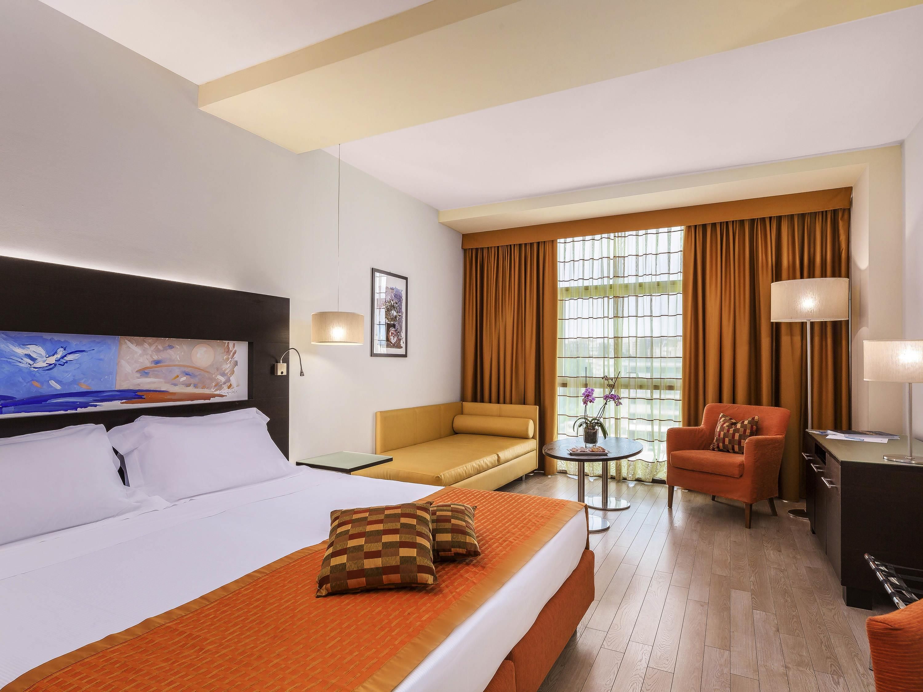 A hotel room with a large bed, a sofa, a chair, a desk, and a window with curtains.