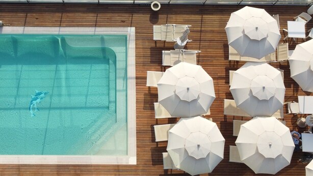 An outdoor swimming pool with a wooden deck, surrounded by white umbrellas and lounge chairs. - Mercure Siracusa Prometeo (Syracuse)