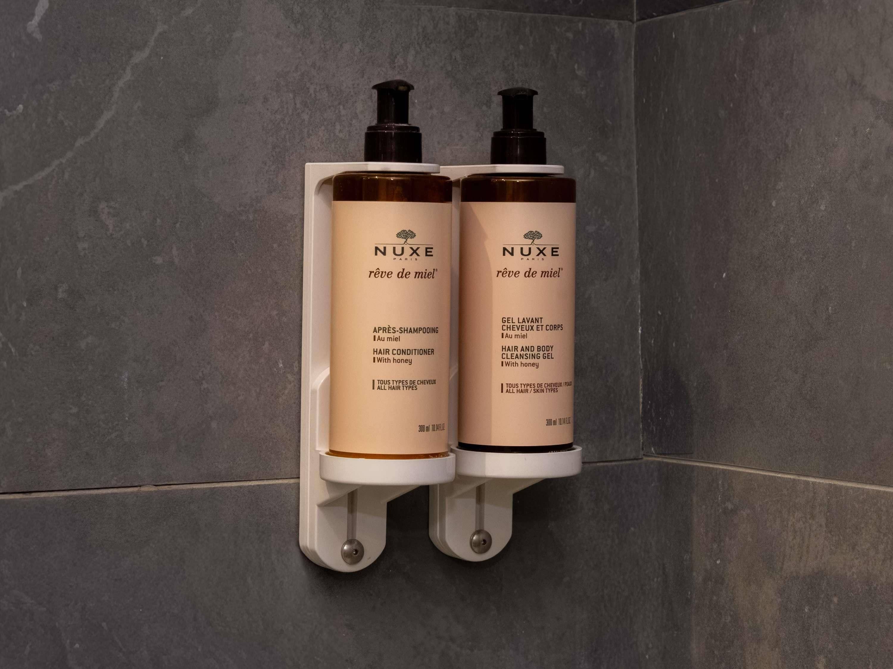 Dos botellas de gel limpiador para cabello y cuerpo NUXE montadas en una pared.