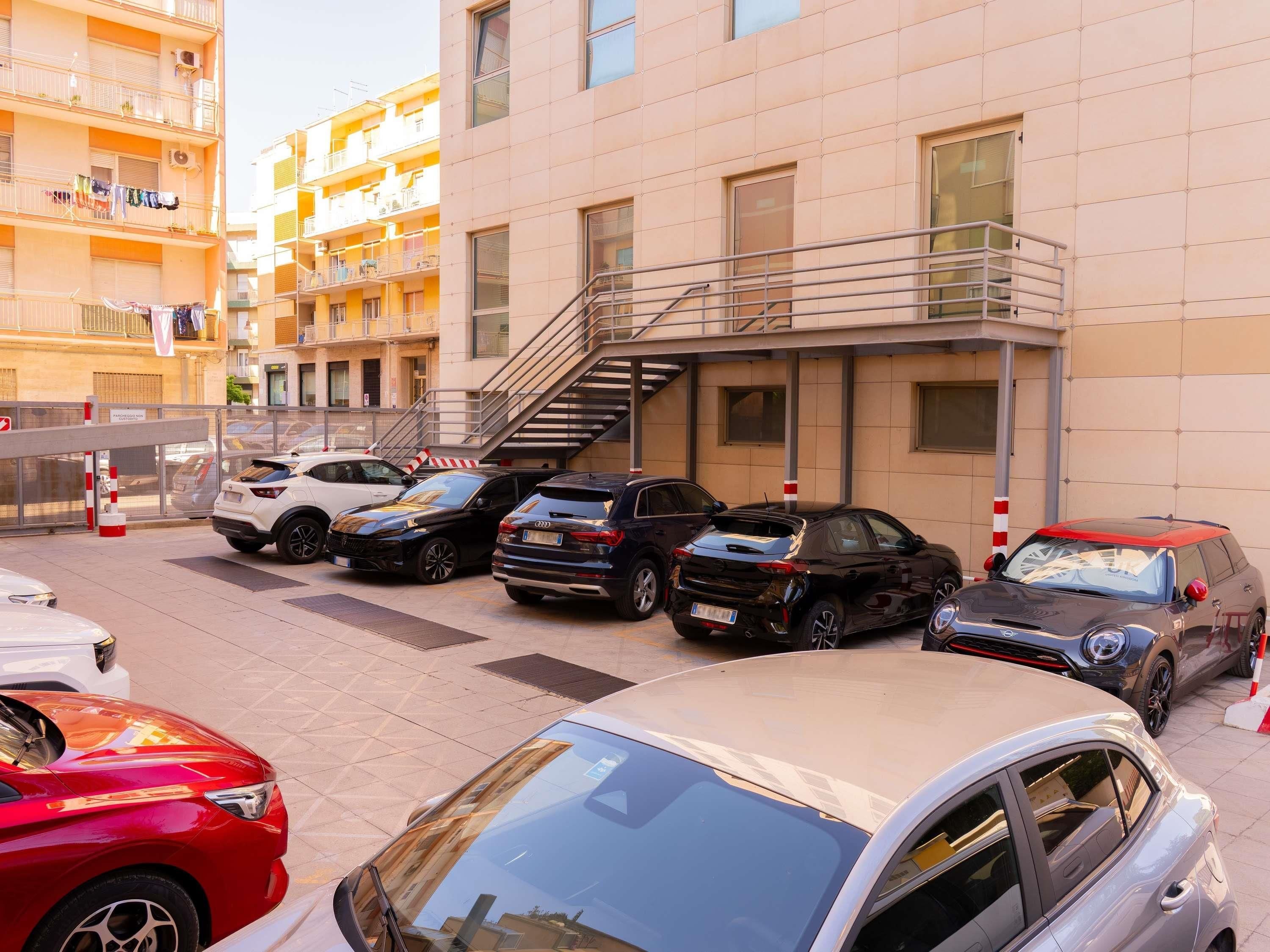Une rangée de voitures garées dans un quartier résidentiel, avec un immeuble à plusieurs étages en arrière-plan.