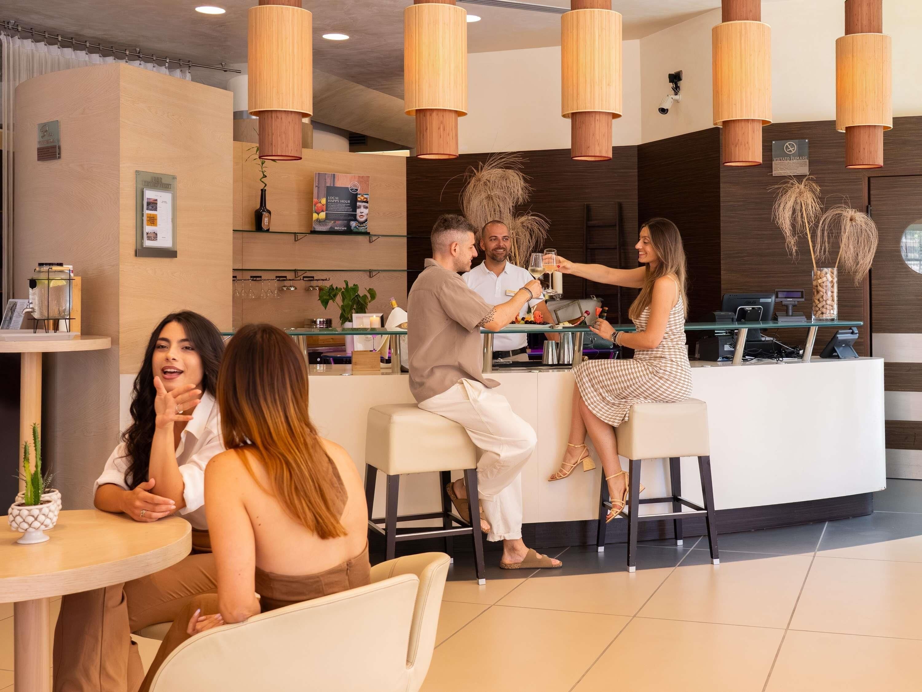 A modern bar area with wooden pendant lighting, a reception desk, and a seating area with a round table.