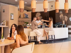 A modern bar area with wooden pendant lighting, a reception desk, and a seating area with a round table. - Mercure Siracusa Prometeo (Syracuse)