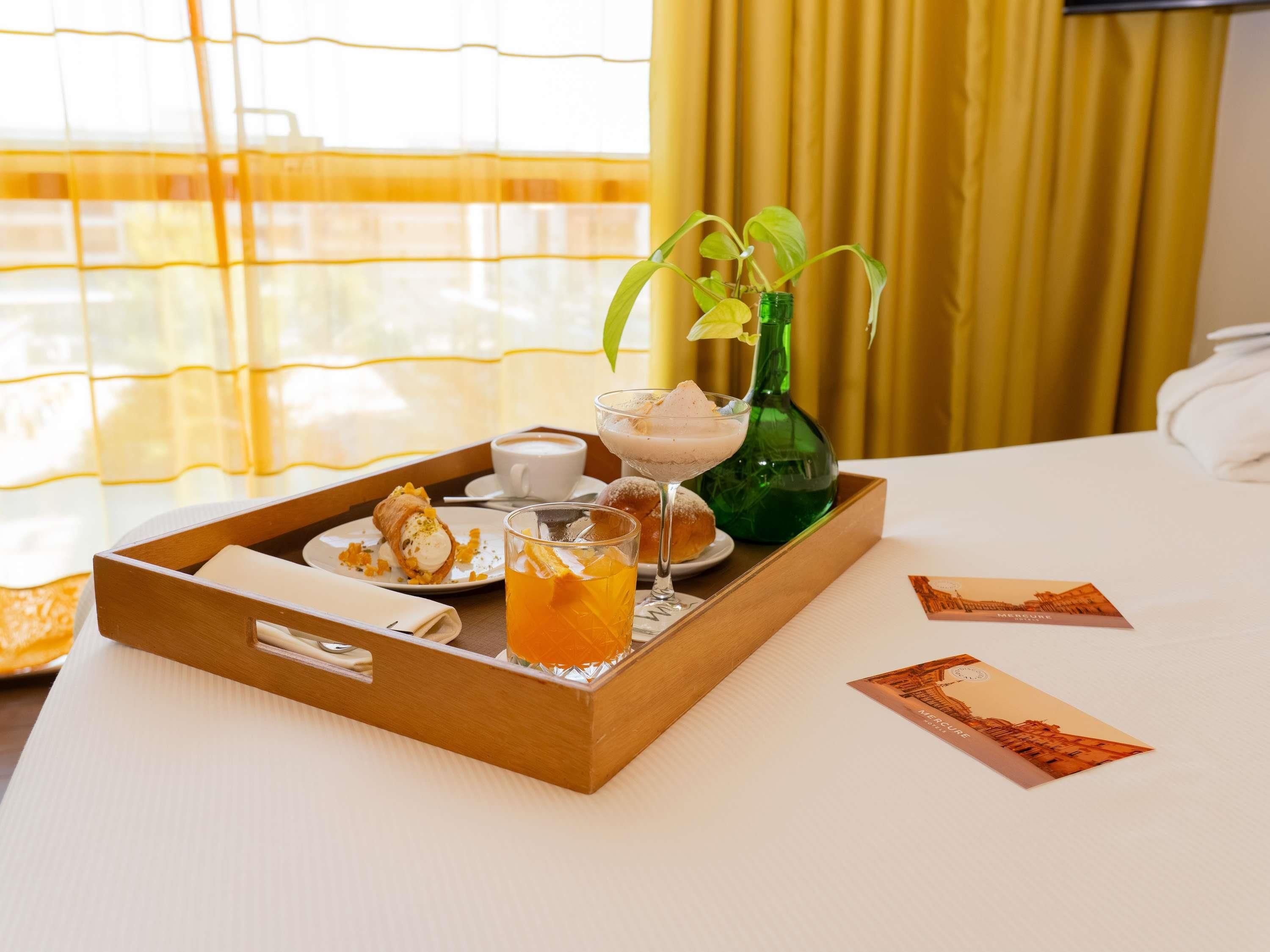 Una bandeja con comida y bebidas sobre una mesa de hotel, una botella verde y una planta.
