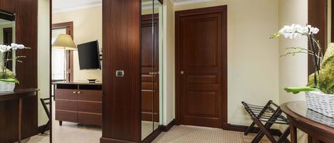 A hotel room with a large mirror, a wooden wardrobe, a television, and a small table with a chair.