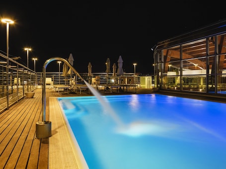 A nighttime pool area with a clear view of the pool, lounge chairs, and umbrellas.. Mercure Siracusa Prometeo