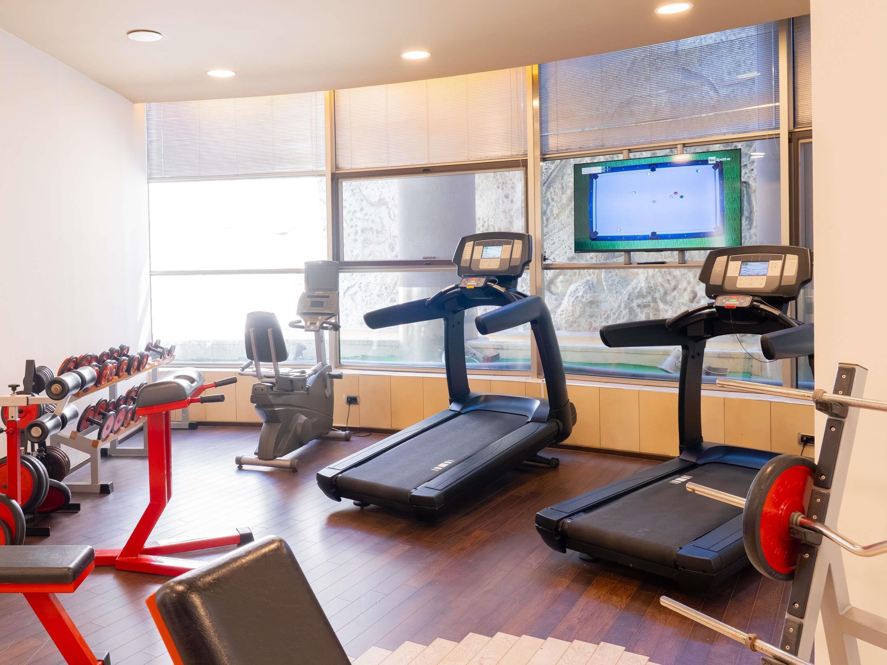 A gym with treadmills, weight machines, and a TV screen.