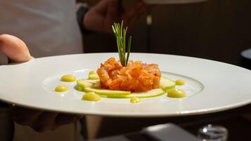 A person holding a white plate with a dish of food, garnished with a sprig of rosemary.