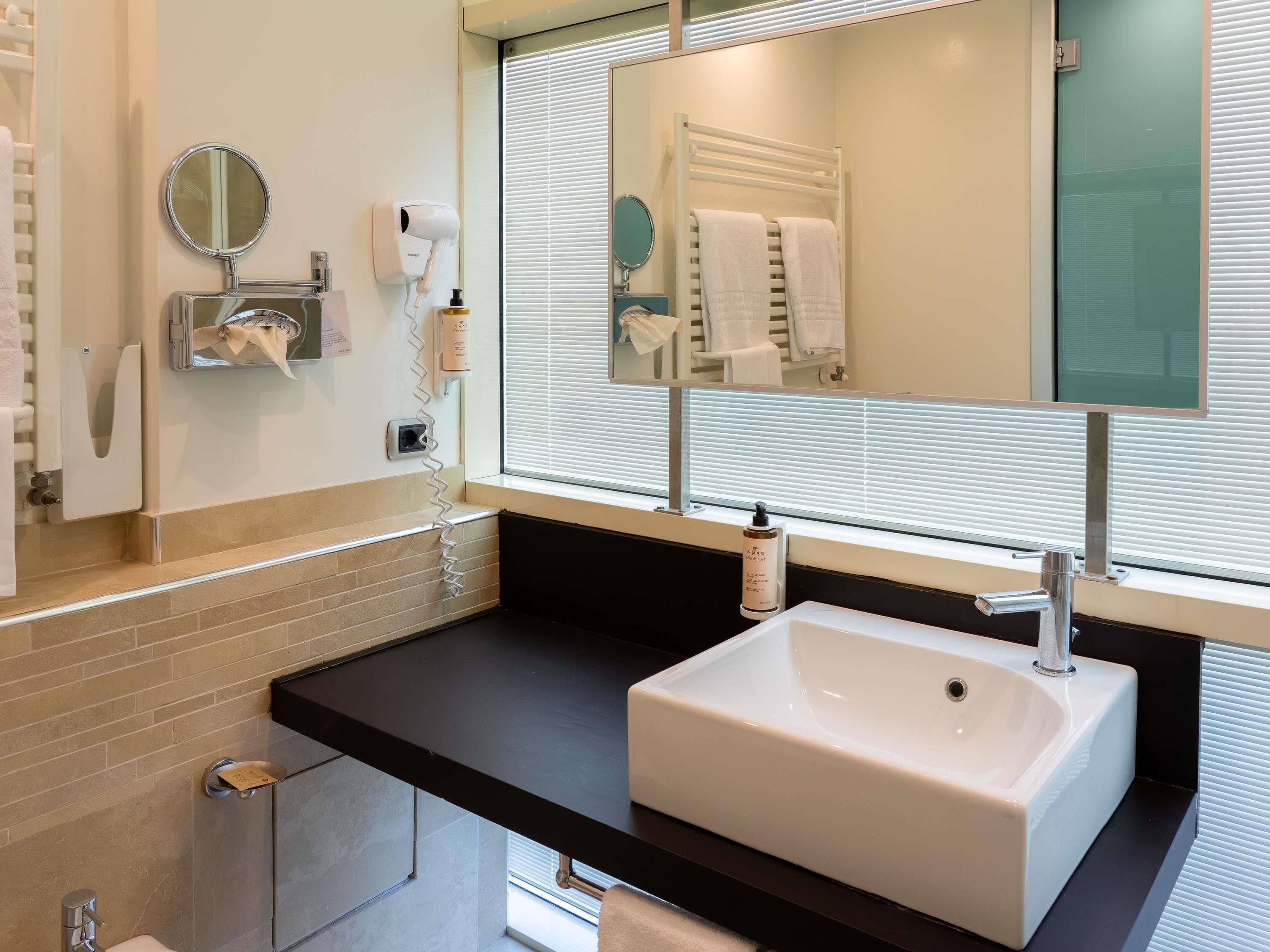 A modern bathroom with a white sink, a mirror, a towel rack, and a hand dryer.