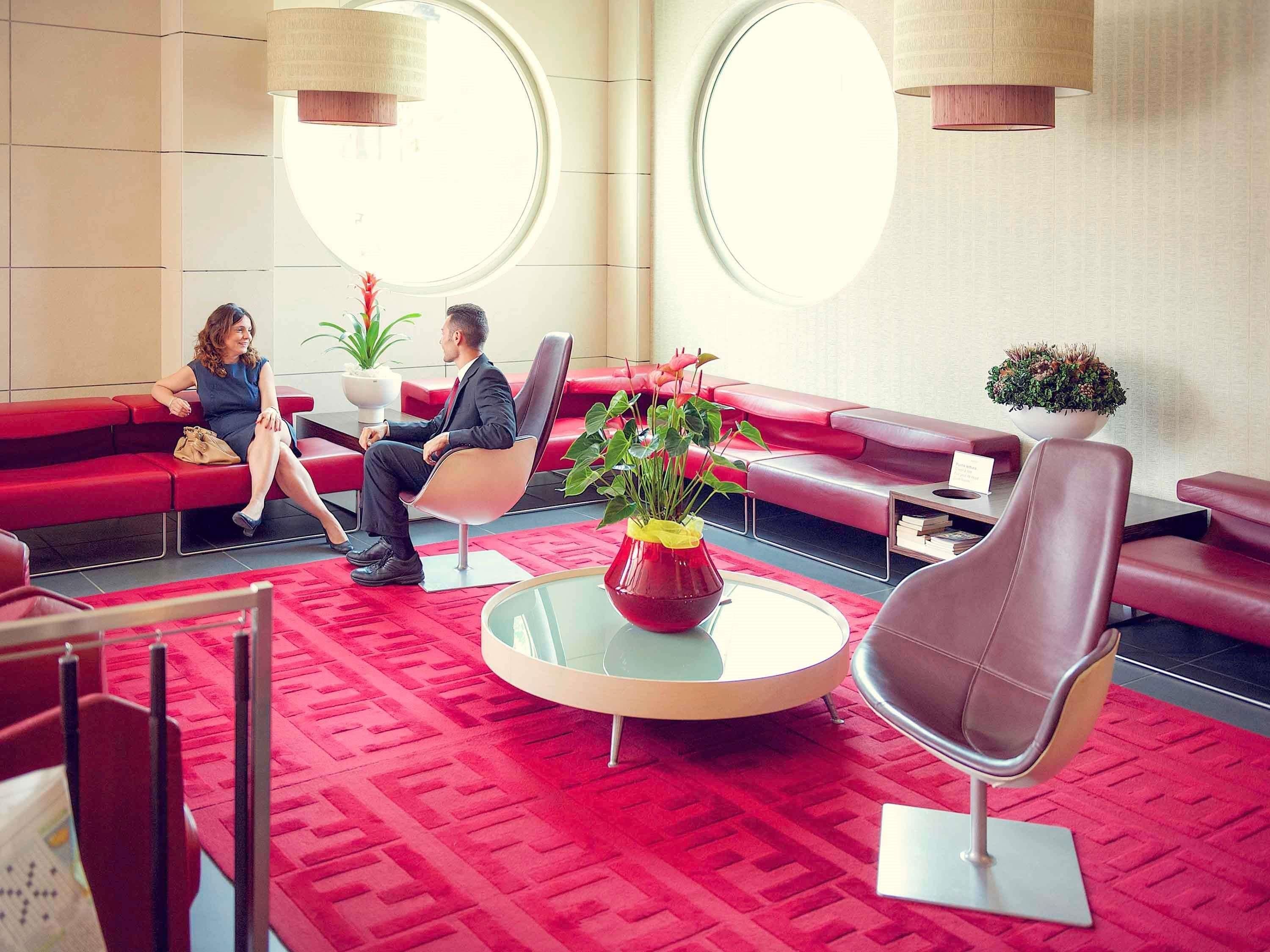 Un moderno vestíbulo con asientos rojos, una mesa de centro de vidrio y plantas en macetas.