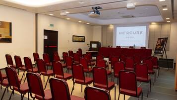 Un salón de conferencias con filas de sillas rojas, una pantalla de proyección y un atril.
