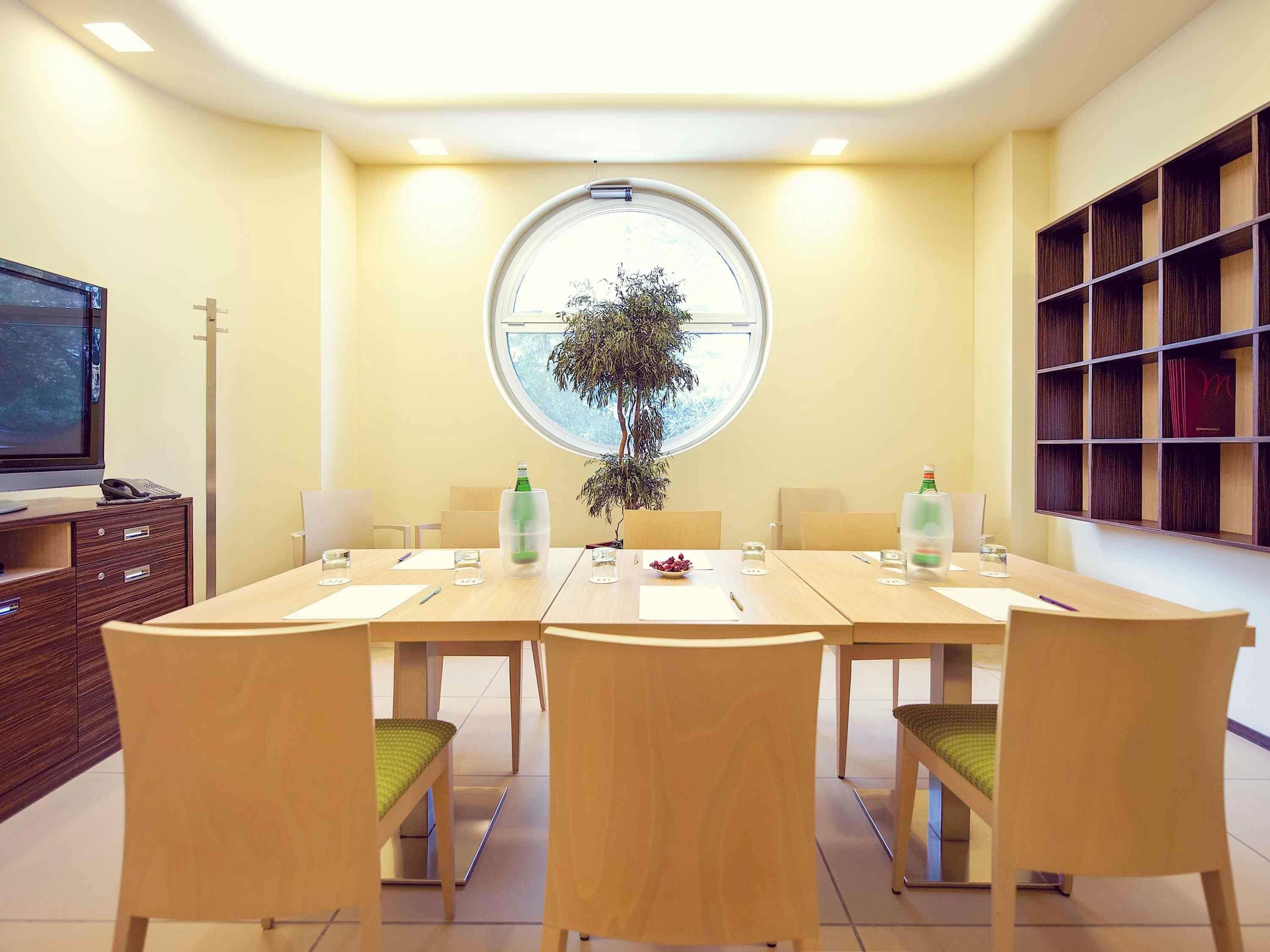 Ein Konferenzraum mit rundem Tisch, Stühlen, einer Pflanze und einem Bücherregal.