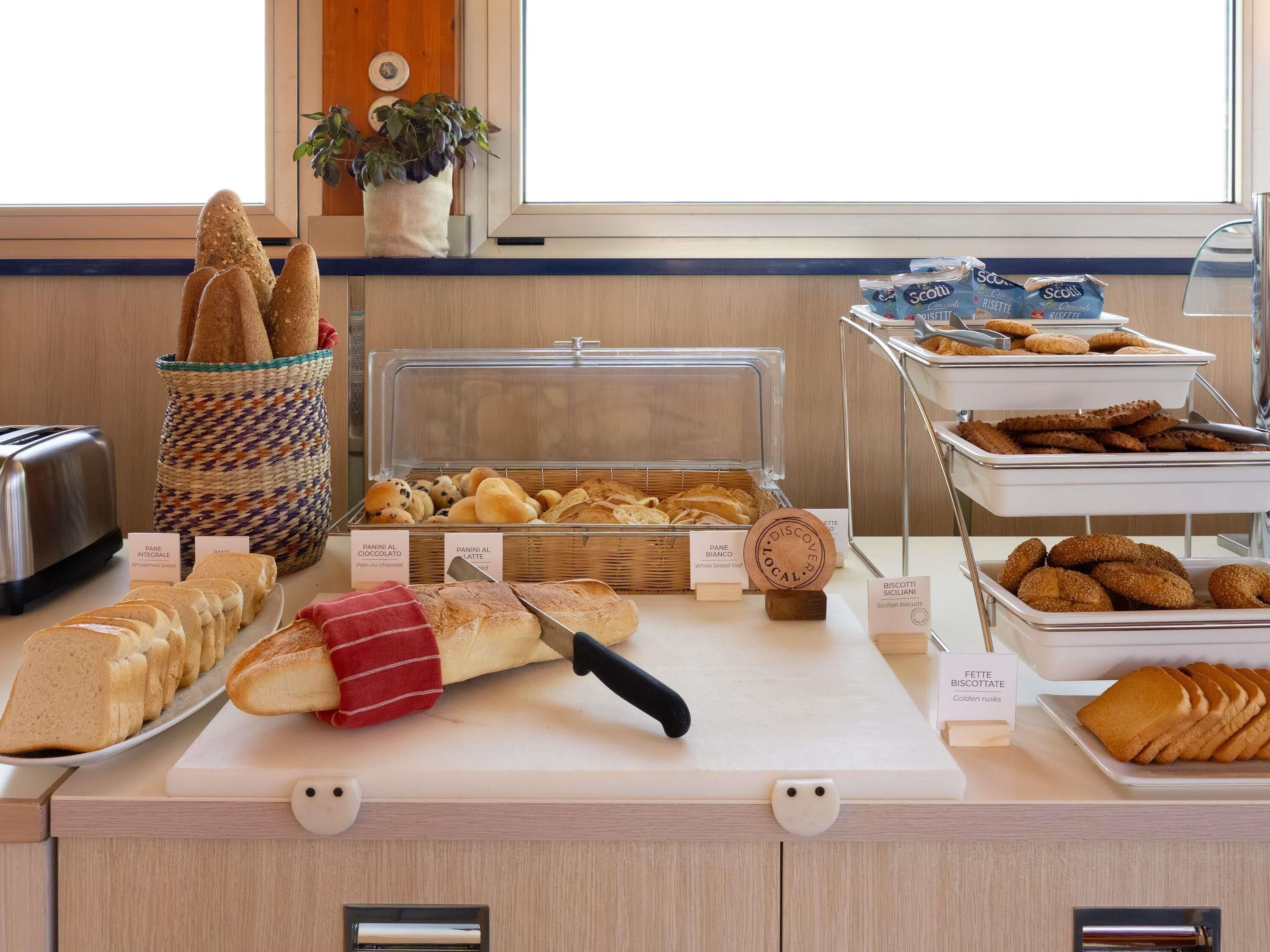 Mostrador de panadería con panes y pasteles variados, incluyendo pan de molde, bollos y biscotti.