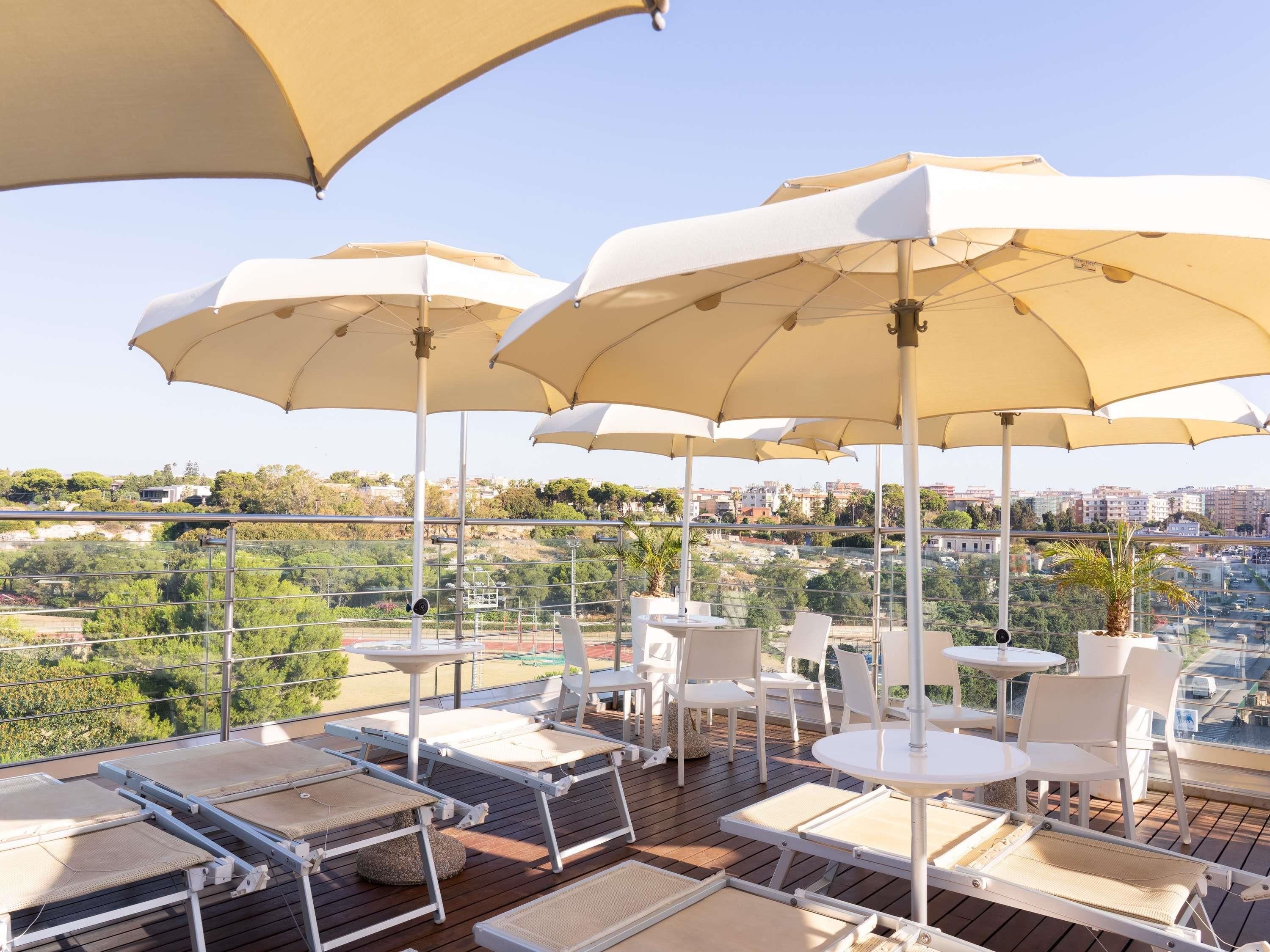 Terraza en la azotea con mobiliario exterior y sombrillas, con vistas a un paisaje urbano.