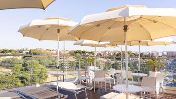 Terraza en la azotea con mobiliario exterior y sombrillas, con vistas a un paisaje urbano.