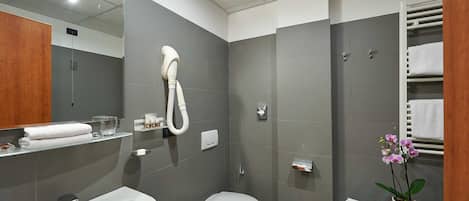 A modern bathroom with a sink, toilet, and shower. There is a towel rack and a small table with a potted orchid.