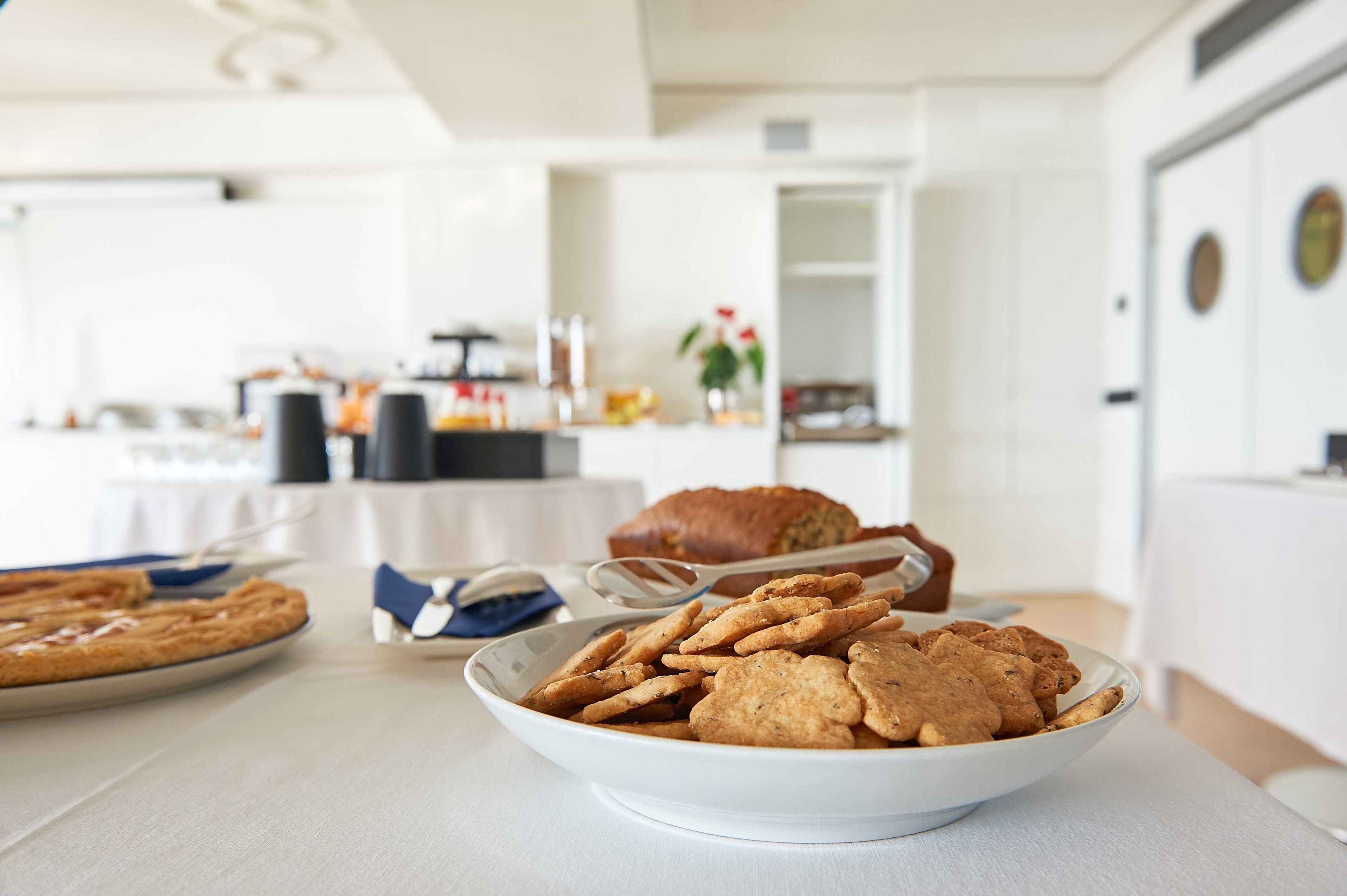 A breakfast buffet with a variety of foods including a large plate of cookies, a loaf of bread, and a pie.