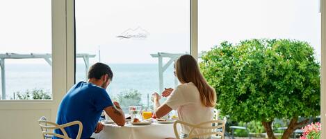 A couple dining at a table with a view of the sea and a logo on the window.