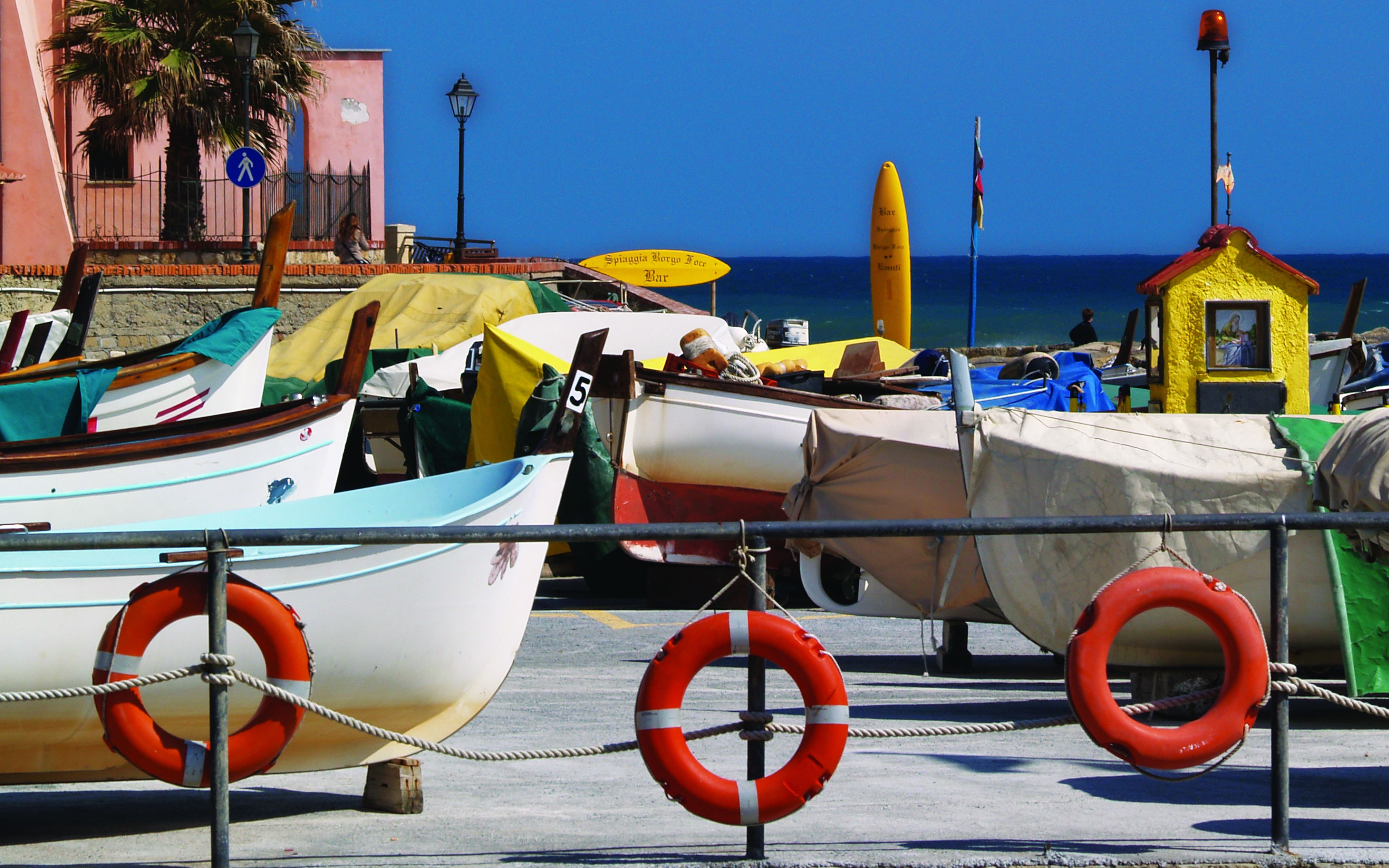Un port de plaisance où sont amarrés plusieurs bateaux, une bouée de sauvetage et un petit bâtiment jaune surmonté d’un drapeau.