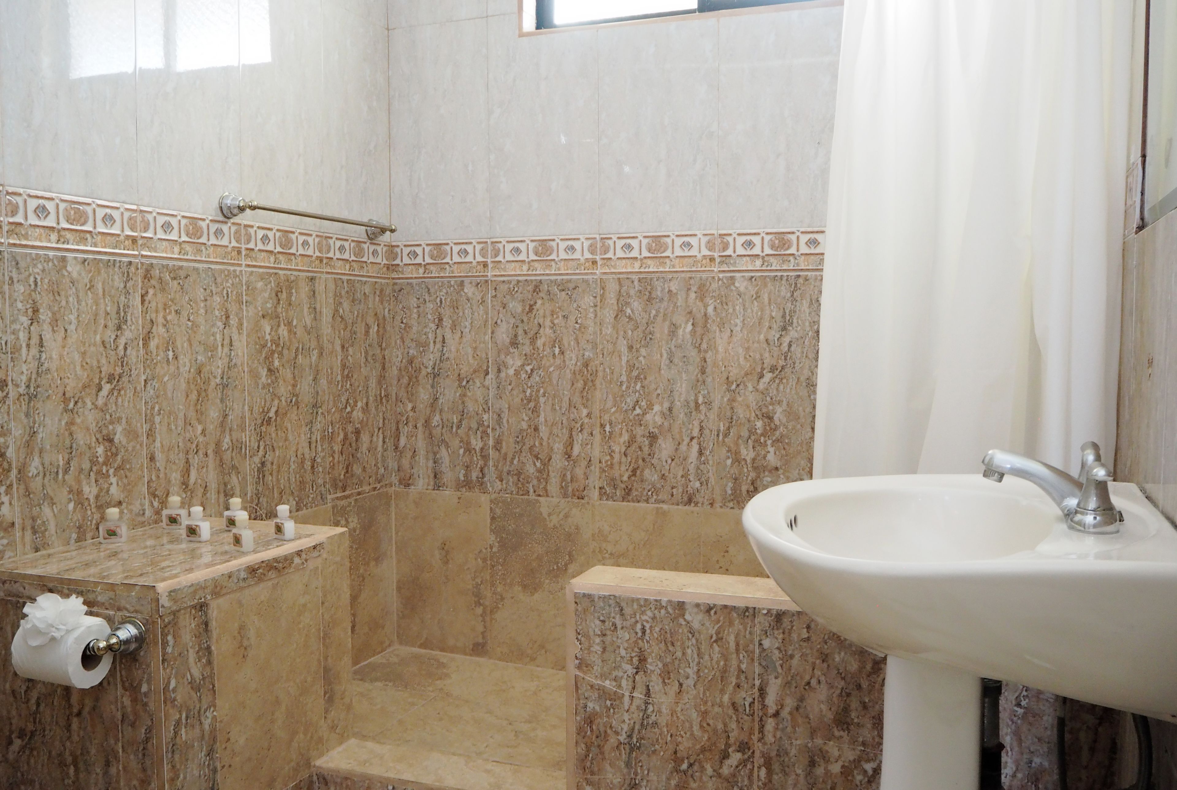 A bathroom with a marble wall, a shower, a sink, and a towel rack.