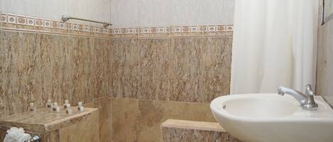 A bathroom with a marble wall, a shower, a sink, and a towel rack.