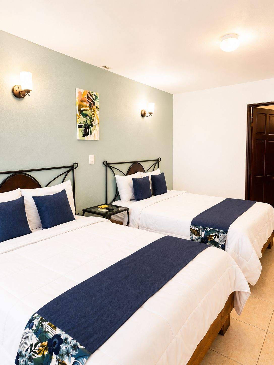 Une chambre d’hôtel avec deux lits, une table de chevet, une lampe fixée au mur et une porte.